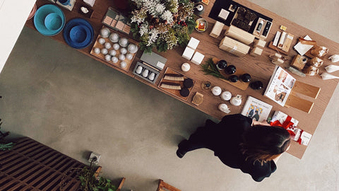 Top-down view of a wooden table with various items and a person standing nearby.